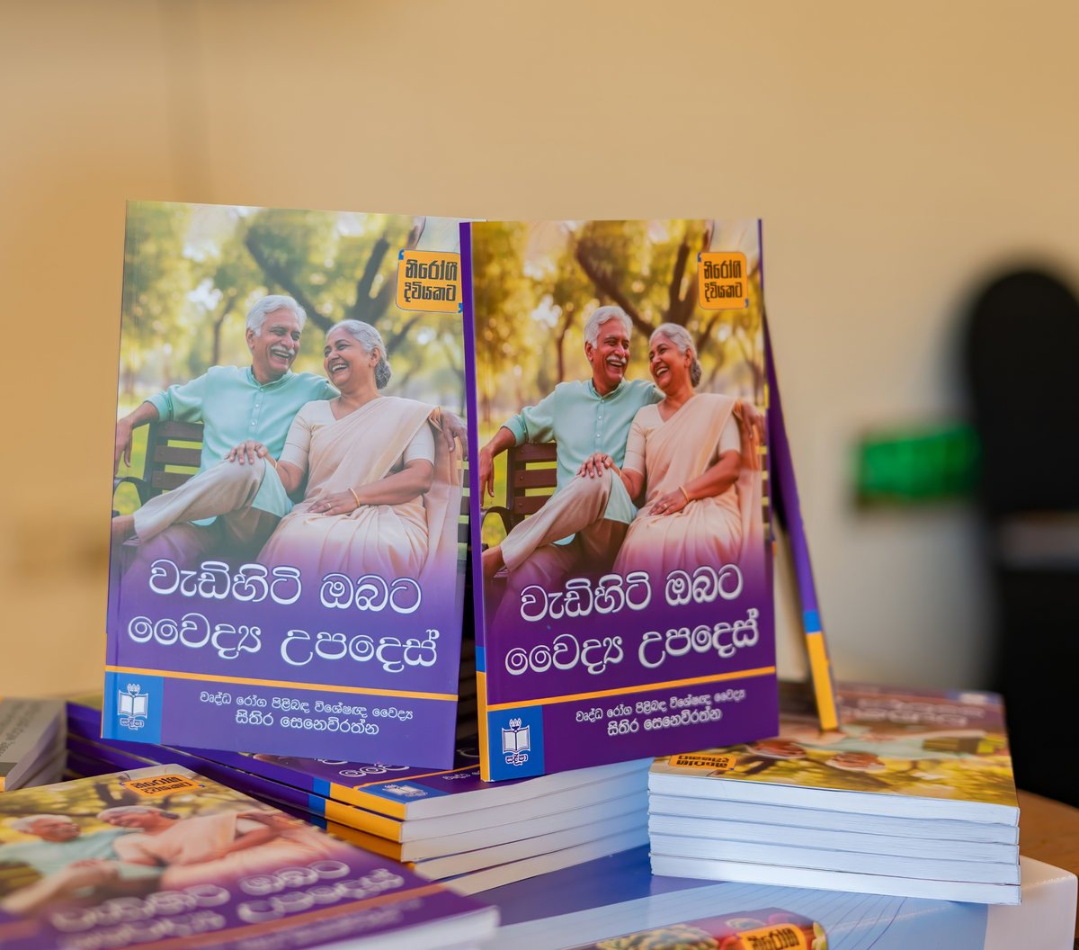 Copies of වැඩිහිටි ඔබට වෙද්‍ය උපදෙස් on the display table at the launch, the cover showing an older Sri Lankan couple on a park bench