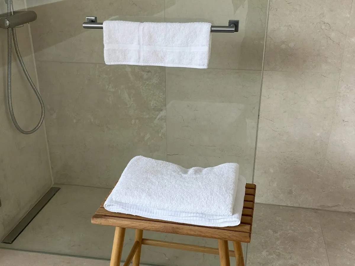 An accessible ensuite shower with a grab rail, a level floor and a teak shower stool
